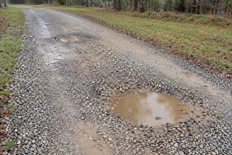 Water-filled potholes in a worn gravel driveway