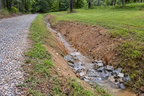 Excavator shaping a drainage swale beside a rural property